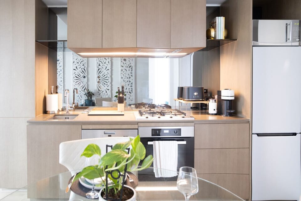 Well-appointed kitchen with warm timber cabinetry, a gas cooktop, Miele oven, dishwasher, and a mirrored splashback reflecting the carved wall panels beyond — fully equipped for guests who enjoy cooking in.