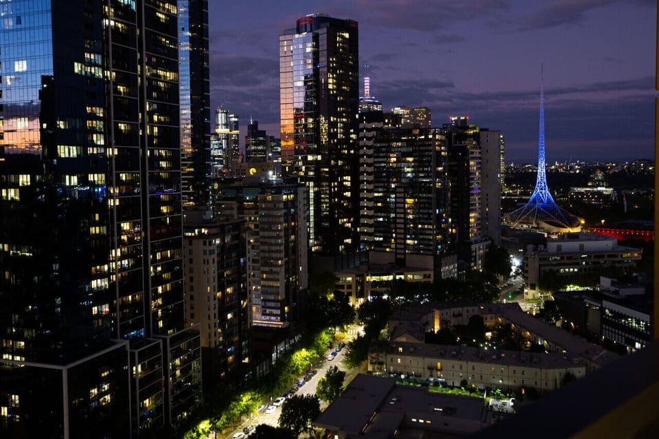 Stunning nighttime view of the Melbourne skyline from the balcony, with city towers, glowing streets, and the illuminated Arts Centre spire visible in the distance — a captivating backdrop after dark.  *(200 characters)*