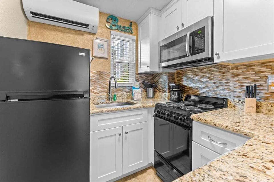 Fully equipped kitchen with granite counters, mosaic tile backsplash, stove, microwave, fridge, coffee maker, and breakfast bar seating — everything you need for a home-cooked meal.