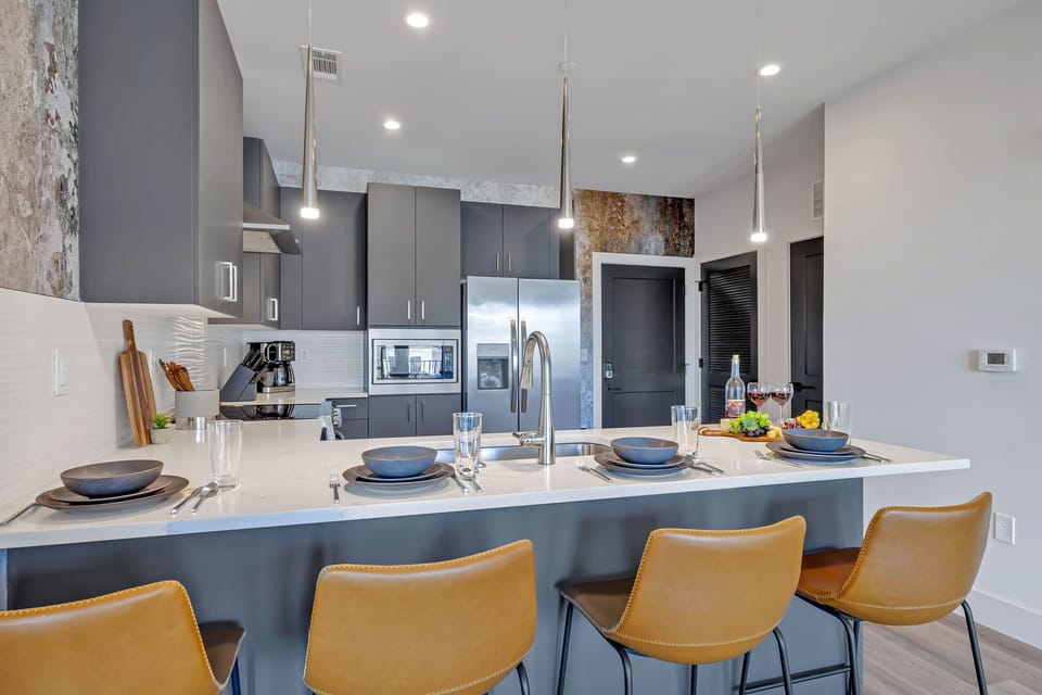 Fully equipped kitchen with stainless steel appliances, basic cooking essentials, coffee machine, and kitchen island seating.