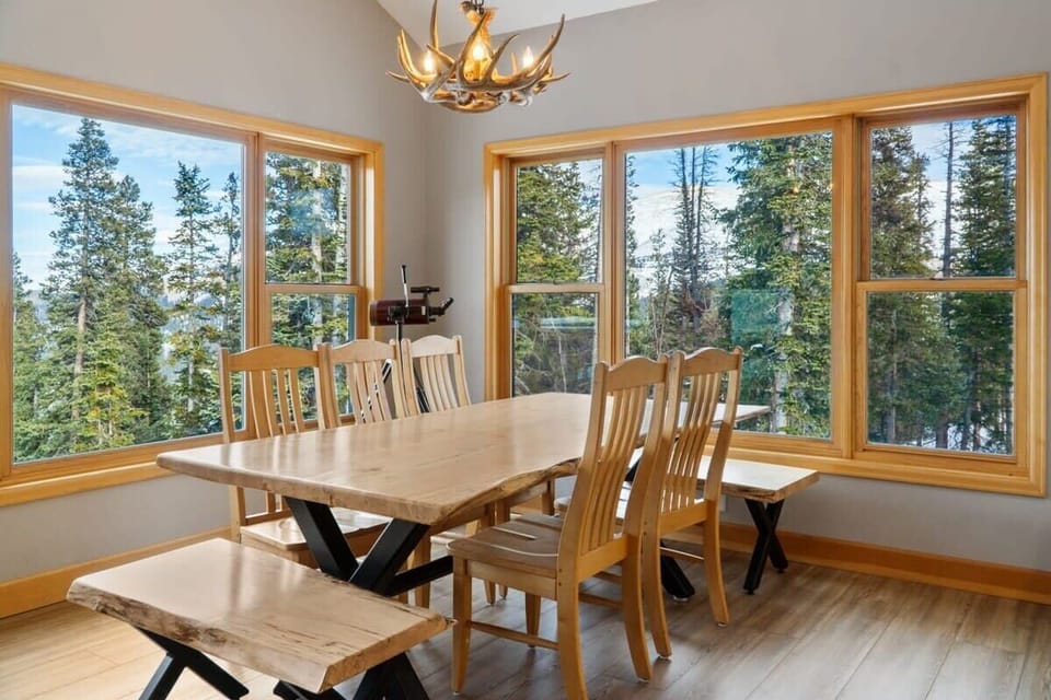 A bright dining room is outfitted with a table with seating for 10 and windows all around framing impressive mountain views.