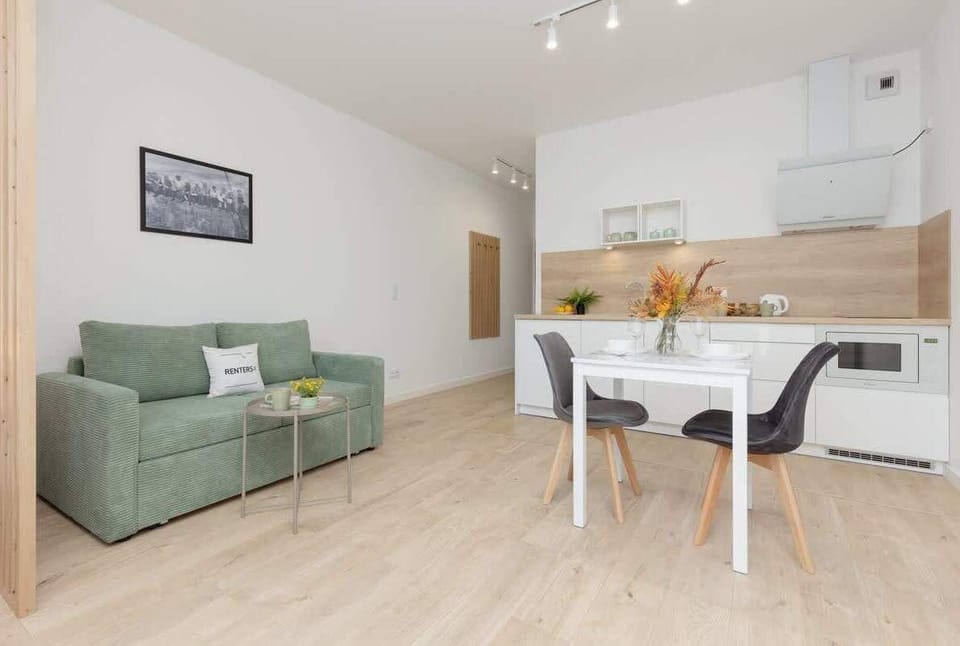 An open-plan living area with a green sofa, a dining table, and a modern kitchen in the background.
