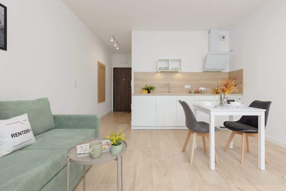 An open-plan living and dining area with a green sofa, bright decor, and a modern TV unit for entertainment.
