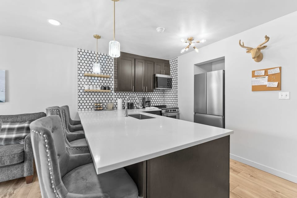 Gather around your stylish kitchen island for meals and conversations in this modern space featuring sleek dark cabinets and striking hexagonal backsplash.