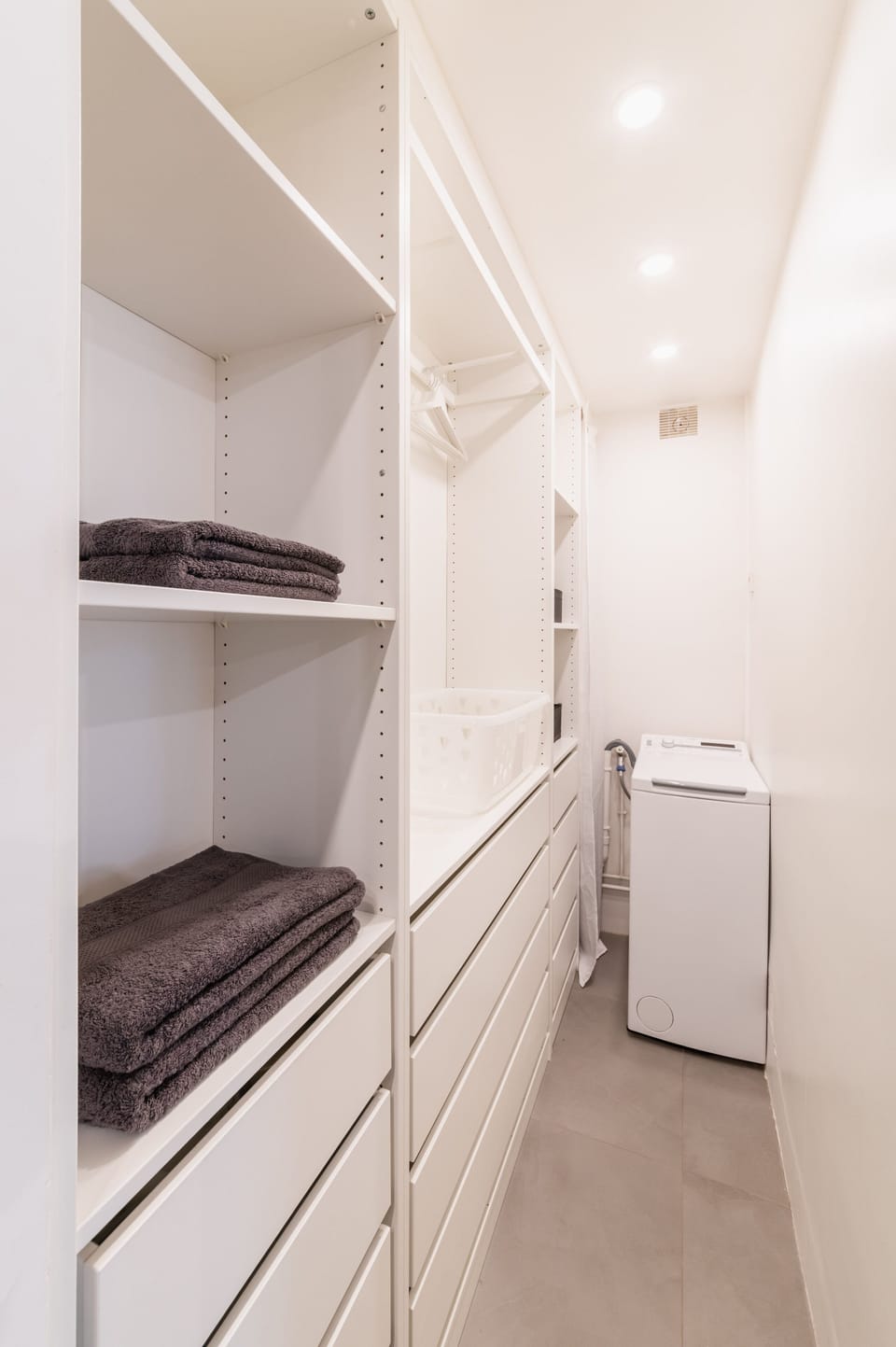A large dressing room with shelves, hangers, iron and washing machine.