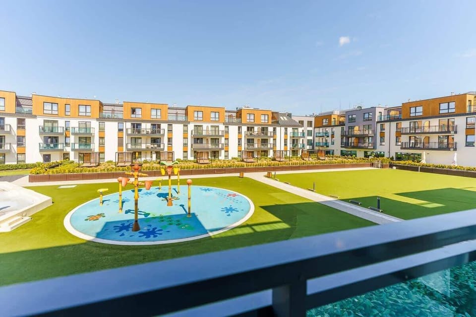 A wide-angle view of a residential complex with a central playground, surrounded by neatly designed buildings.








