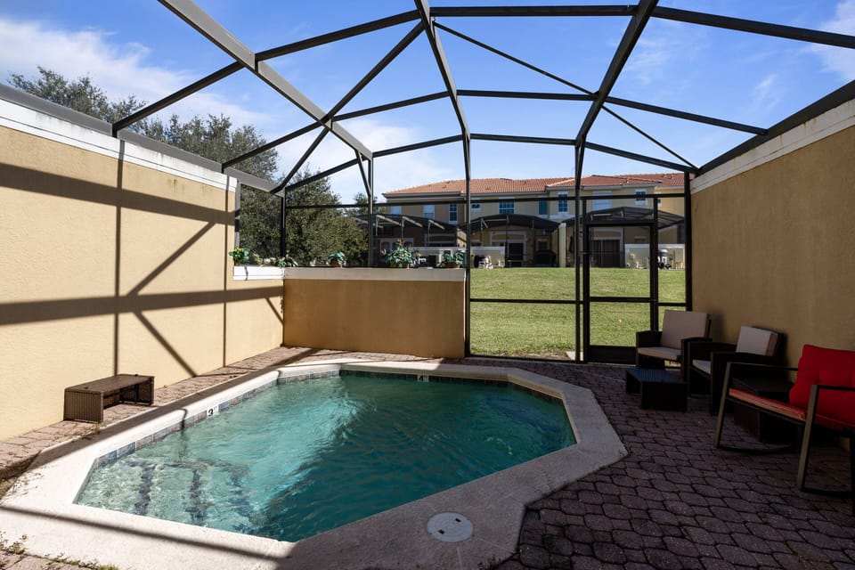 Discover your private oasis with a delightful octagonal pool and a spacious tiled patio. Unwind on modern outdoor seating while sunlight filters through the screened enclosure, providing a serene view of the lush greenery.