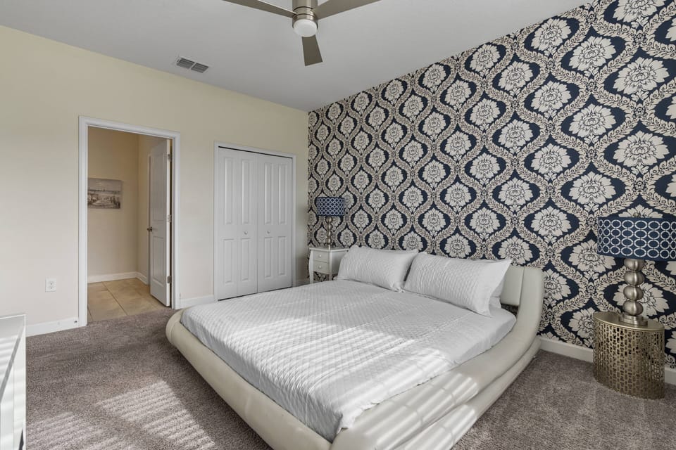 Step into this stylish bedroom, where soft, neutral tones harmonize with a striking blue patterned accent wall. The plush carpeting invites you to sink in, while the sleek bed offers a cozy oasis for restful nights.
