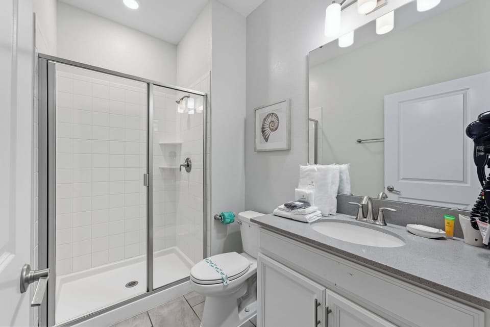 Enjoy a bright, airy bathroom with sleek gray countertops and a spacious walk-in shower with clear glass doors, offering a refreshing start to your day. Soft white towels and minimalist decor enhance the inviting atmosphere.