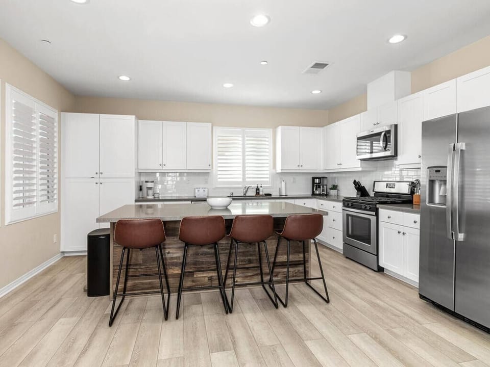 White wooden kitchen w/stainless steel appliances and large island
