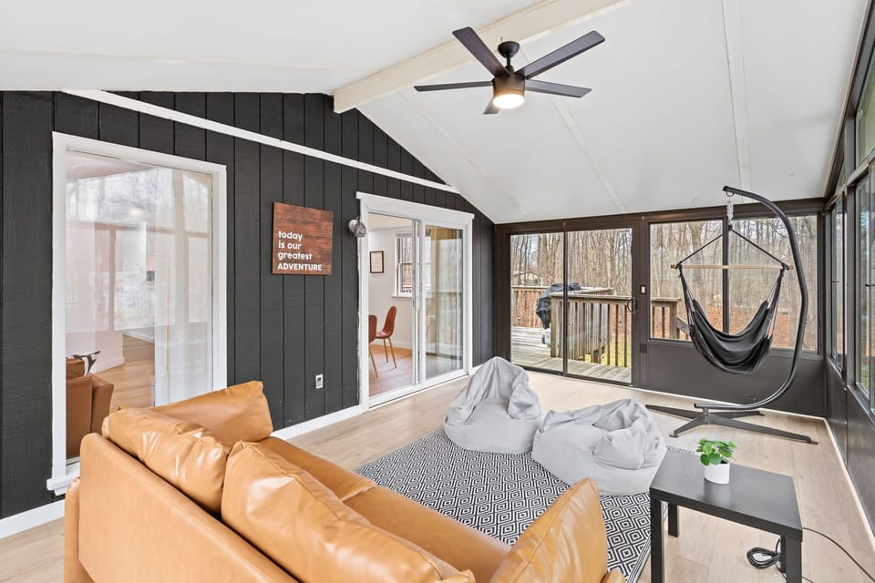 This stylish sunroom is the perfect place to unwind, featuring a cozy leather couch, bean bag seating, and a swinging hammock chair, all with a beautiful view of the outdoors.
