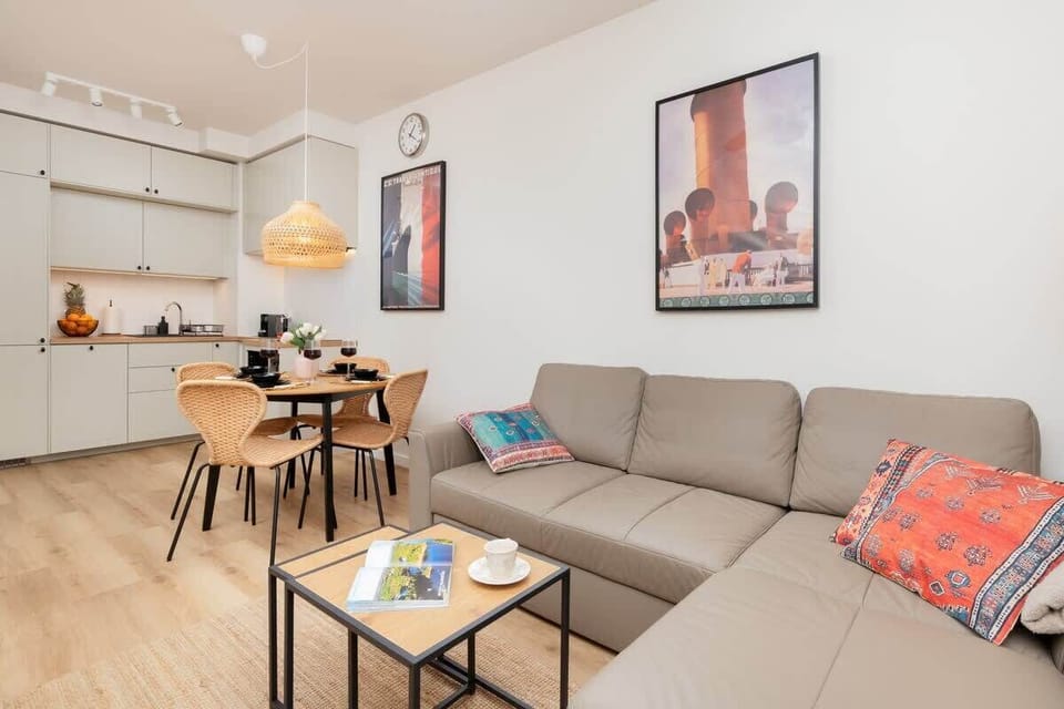 Another view of the living room, showcasing a wooden dining table with chairs, a beige sofa, and a bright, airy space.
