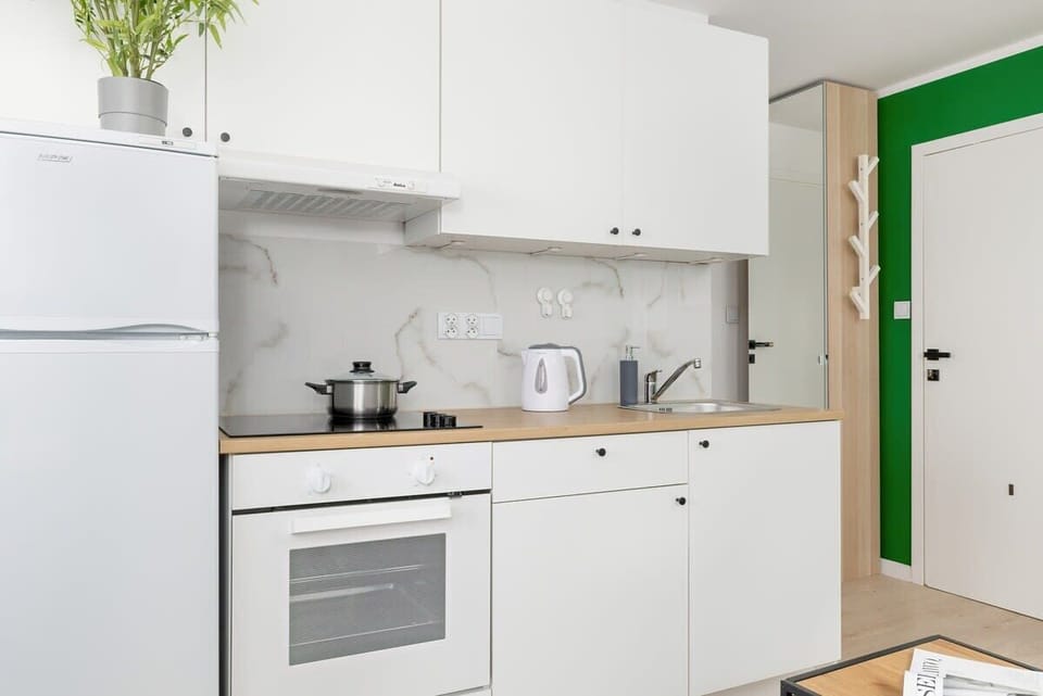 A modern kitchen with white cabinets, a green accent wall, and small potted plants.