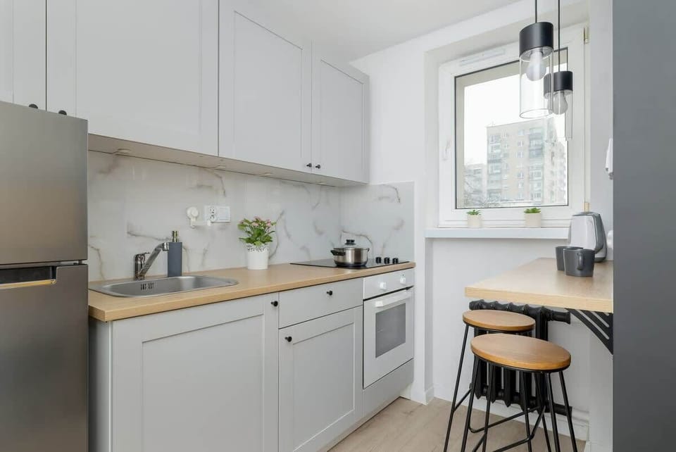 A bright kitchen with white cabinets, a small dining table, and a large window letting in natural light.