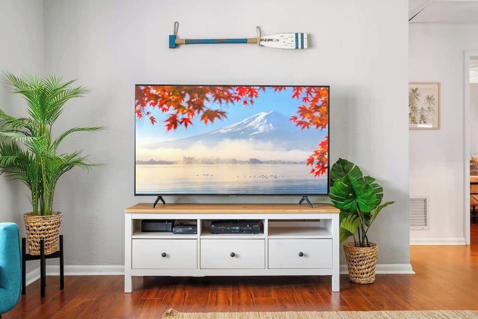 Enjoy entertainment and comfort in this inviting living room. Smart TV, stylish media console, warm wood floors, and coastal accents—perfect for movie nights, streaming your favorites, or relaxing indoors after a sunny day by the pool.