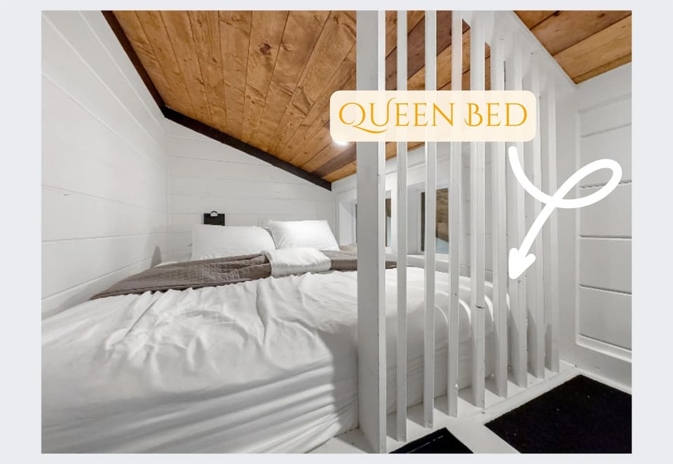 Slip into comfort in our charming loft bedroom, featuring a plush queen bed nestled under a rustic wood-paneled ceiling. It's your private haven for a restful night's sleep.