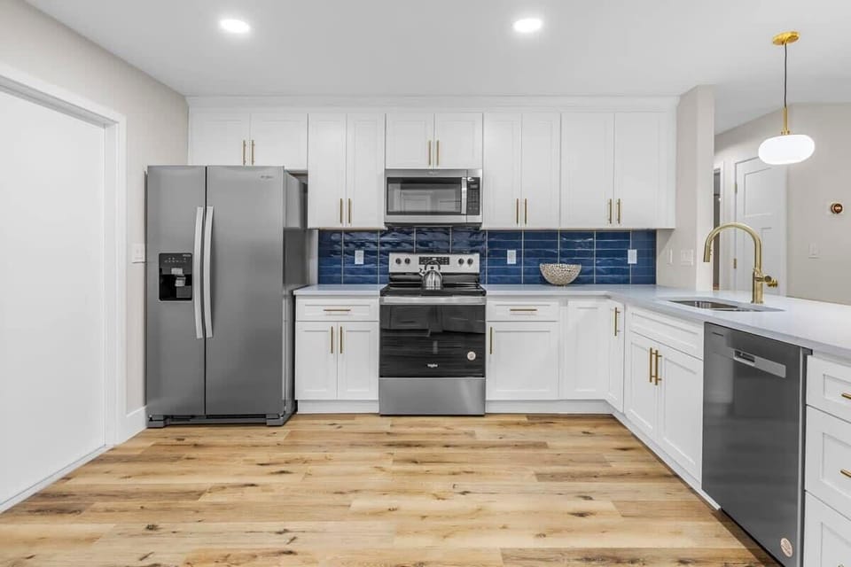 Modern kitchen with white cabinetry, blue tile backsplash, and stainless steel appliances.