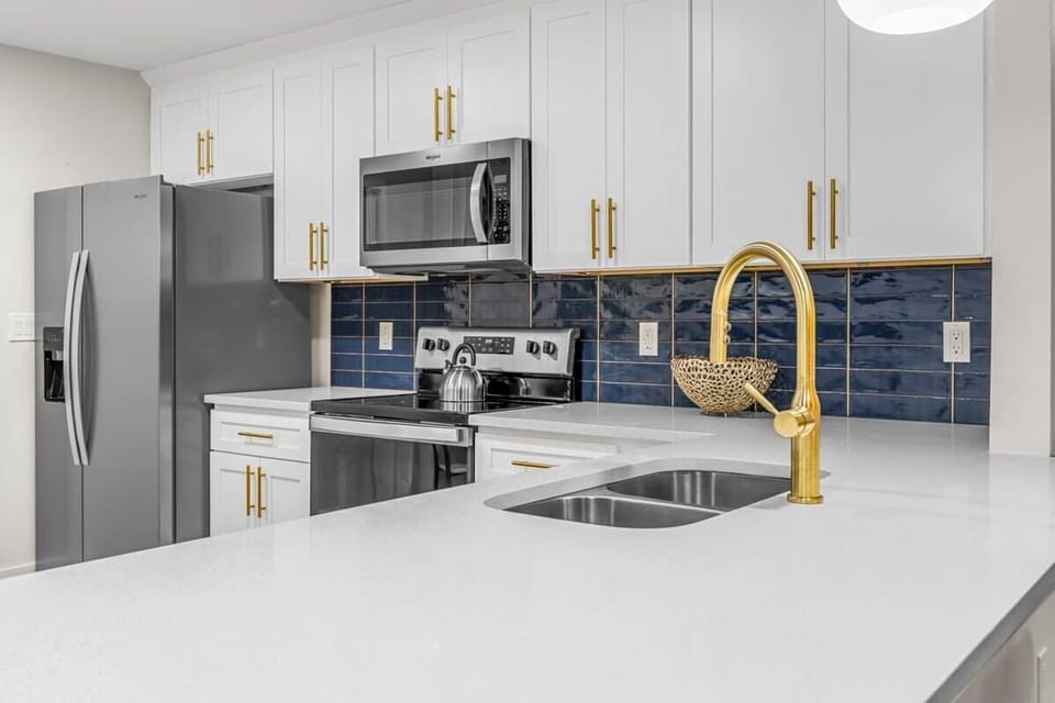 Modern kitchen with white cabinetry, navy tile backsplash, and gold fixtures.