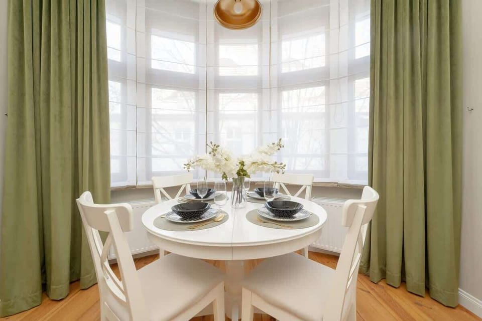 A cozy dining area near a window, with a small round table and green curtains.