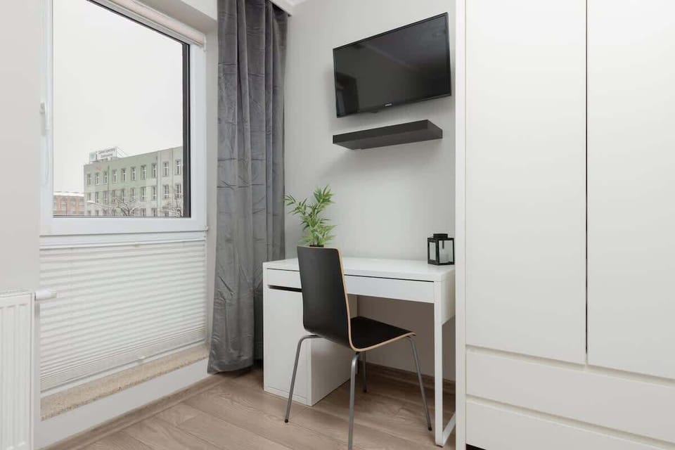 Another view of the bedroom, showing a wardrobe and a workspace with a desk and chair near a window.