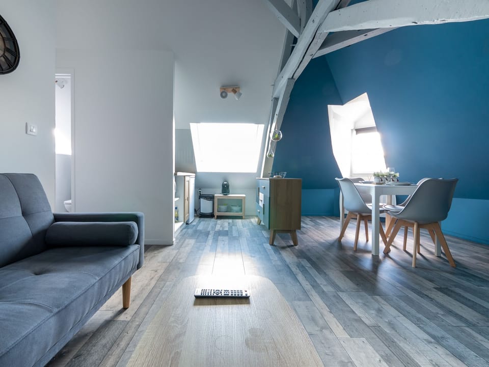 "This open kitchen is bathed in natural light thanks to a well-placed window. The white and blue walls create a bright atmosphere. The kitchen is functionally equipped, with a comfortable seating area nearby. The dining room is also integrated into this room, promoting conviviality during meals. This space combines functionality, brightness and style."