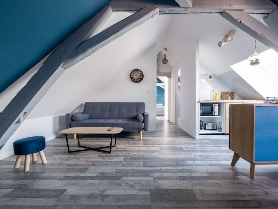 "This open kitchen is bathed in natural light thanks to a well-placed window. The white and blue walls create a bright atmosphere. The kitchen is functionally equipped, with a comfortable seating area nearby. The dining room is also integrated into this room, promoting conviviality during meals. This space combines functionality, brightness and style."