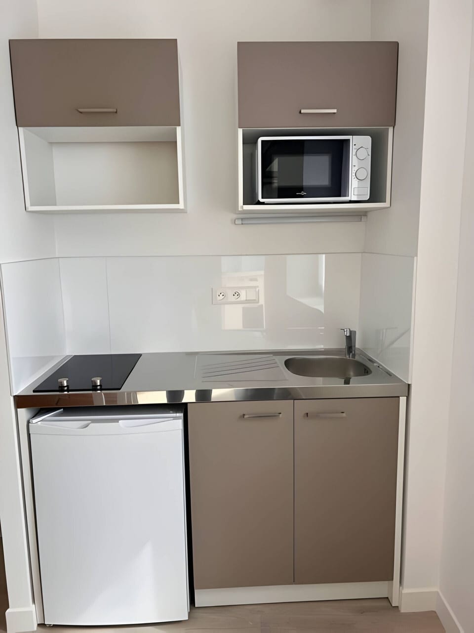 "Discover the functional kitchenette in the "Le Donjon" apartment with its simple stainless steel sink, small refrigerator, microwave oven and storage units. Enjoy a practical space for preparing your meals and eating out."