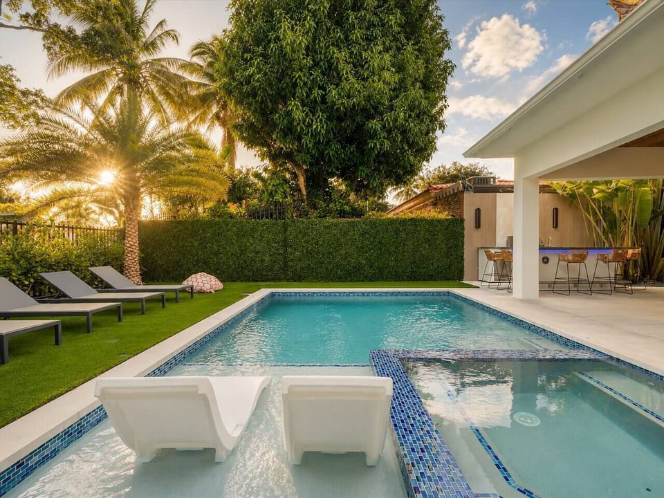 Two white lounge chairs sit partially submerged on the shallow tanning ledge of your private pool. Relax in the integrated hot tub or lounge on the poolside chairs under the shade of tropical palm trees in Coconut Grove.