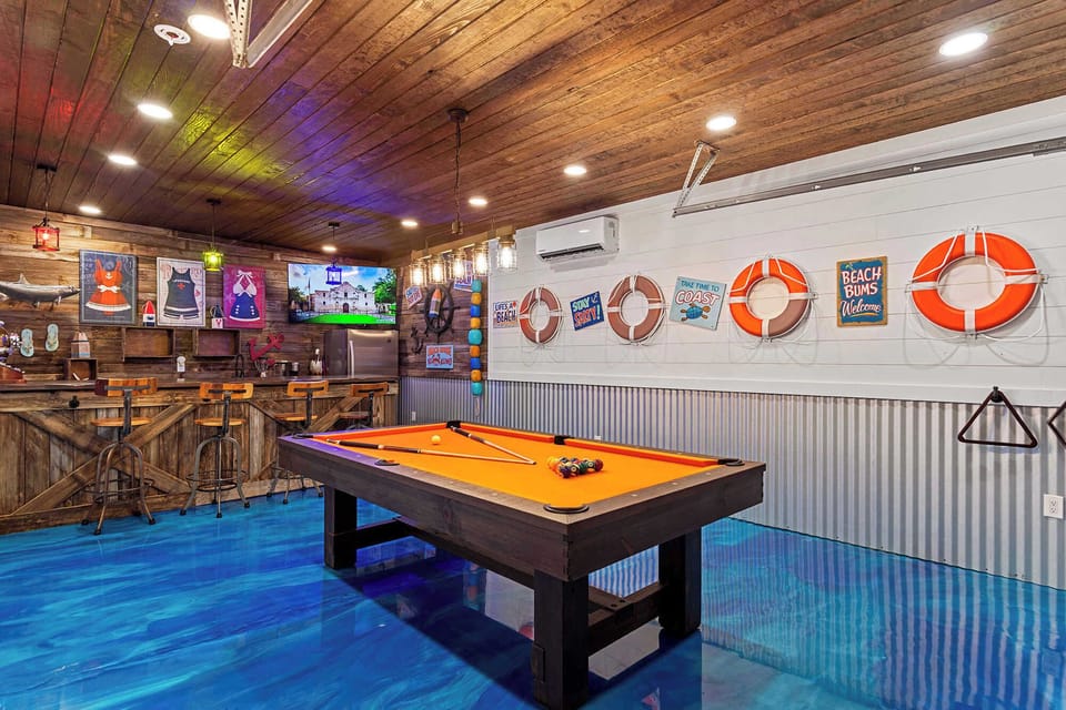 Lively game room featuring a pool table, bar seating & colorful coastal decor.