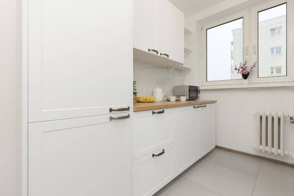 A sleek, all-white kitchen with modern appliances, ample storage, and a large window providing daylight.