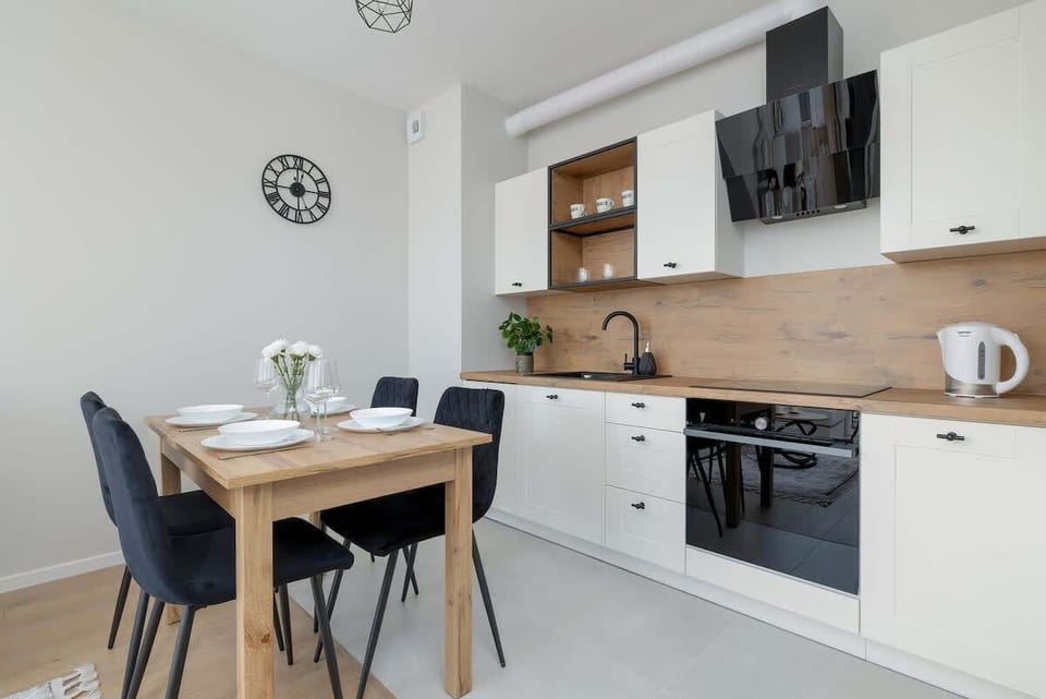 A modern kitchen with white cabinets, a wooden countertop, and a dining table with chairs.