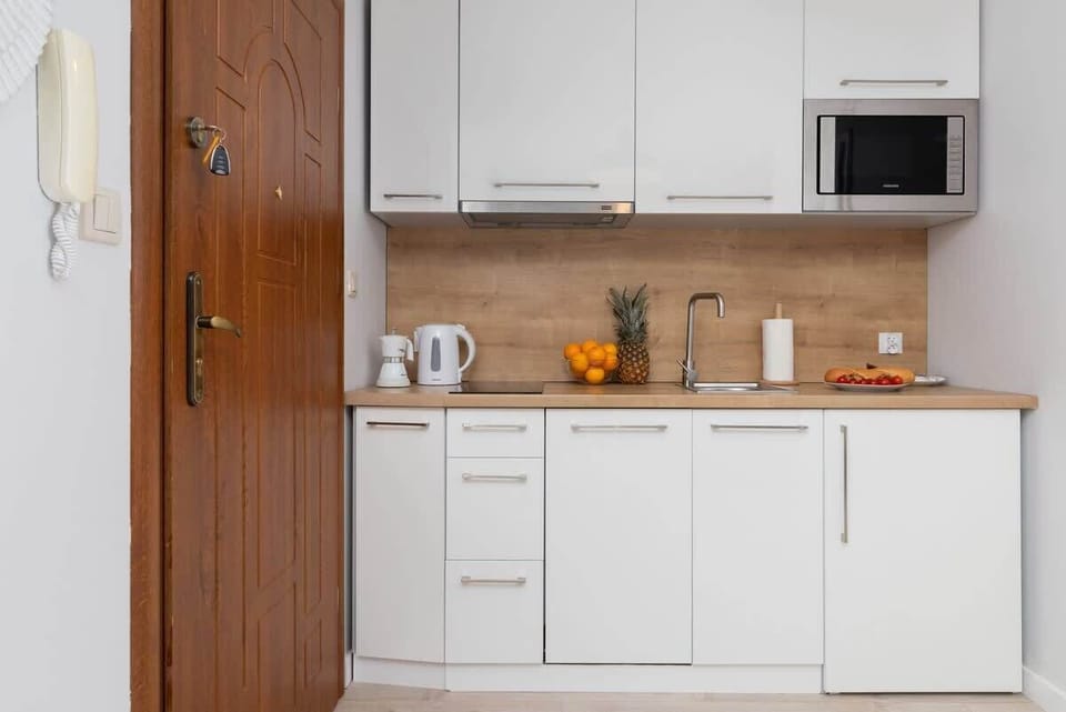 A compact kitchenette with white cabinets, a wooden countertop, and modern appliances, offering functionality.

