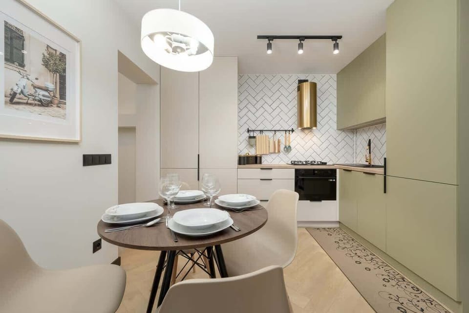 A stylish dining area with a round table set for four, adjacent to a modern kitchen with light green cabinetry.
