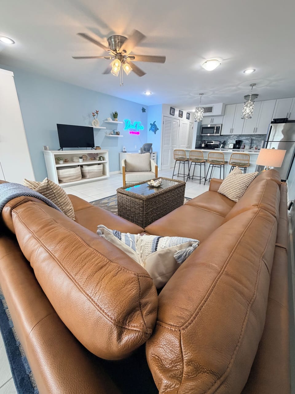 Living room open to kitchen. Roku tv, leather couch, desk with chair.