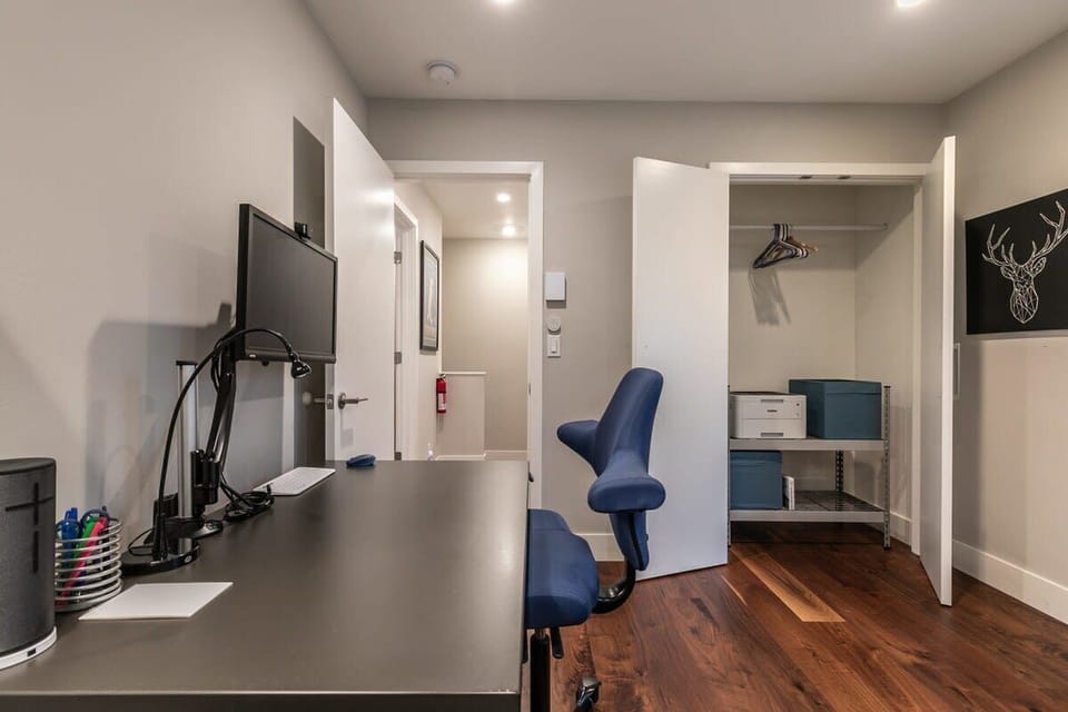 The second bedroom is a dynamic room set up for rest or work with a twin-size bed and a workspace with an adjustable desk, chair, and monitor.