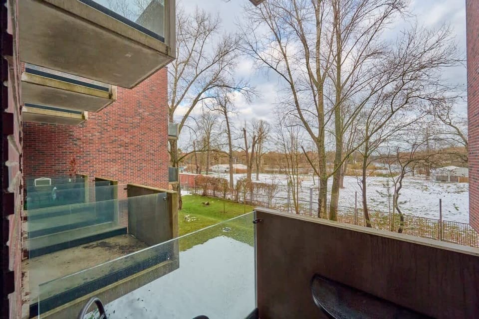 A balcony view overlooking a picturesque river surrounded by leafless trees, showcasing the serene natural setting. The modern glass railing adds a contemporary touch to the architectural design.
