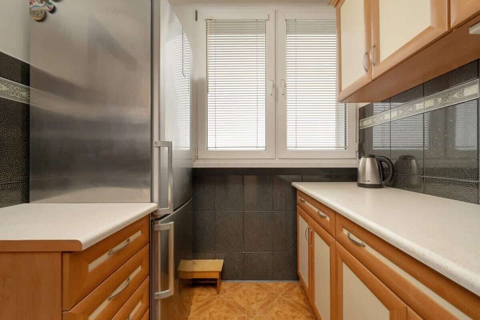 A compact kitchen with wooden cabinets, stainless steel appliances, and a window for natural light, offering a functional cooking space.

