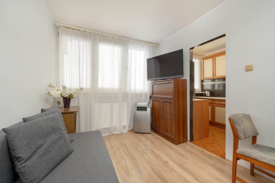 A seating area with a gray sofa, a wooden cabinet, and large windows with white curtains, providing a comfortable lounge spot.

