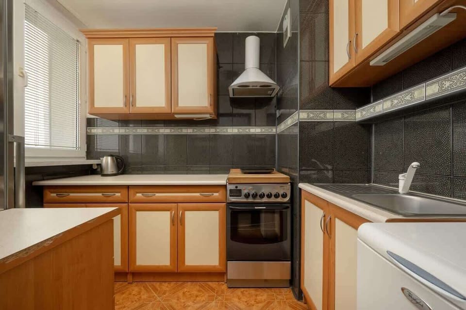 A close-up of the kitchen with wooden cabinets, a gas stove, and a window for ventilation, ensuring a practical cooking area.

