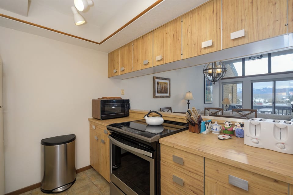 Cook with ease in your fully equipped kitchen featuring warm wood cabinets, modern appliances, and mountain views through the window.