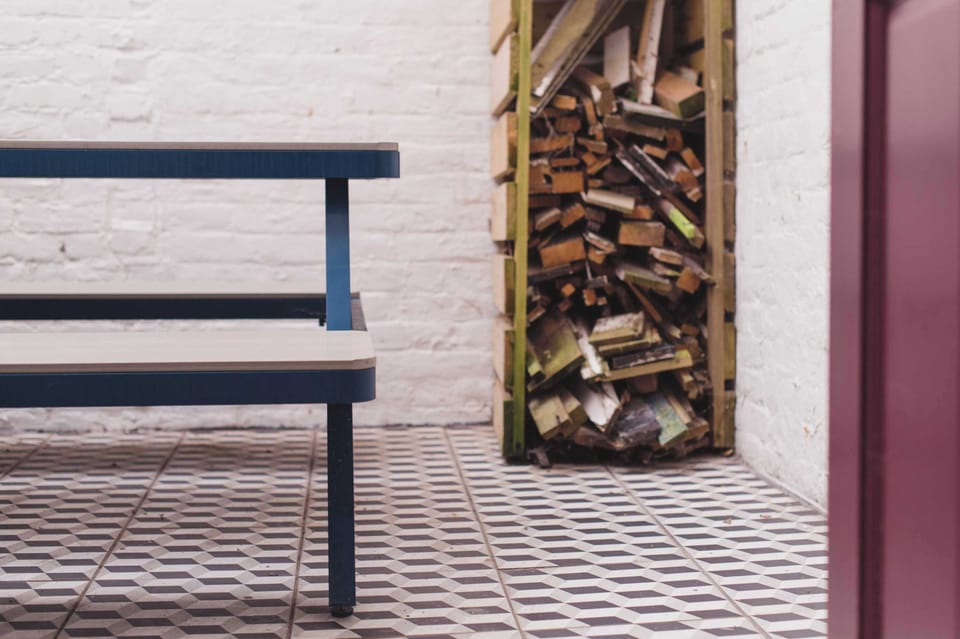 A rustic yet modern outdoor space with a blue bench, wood storage, and stylish flooring.