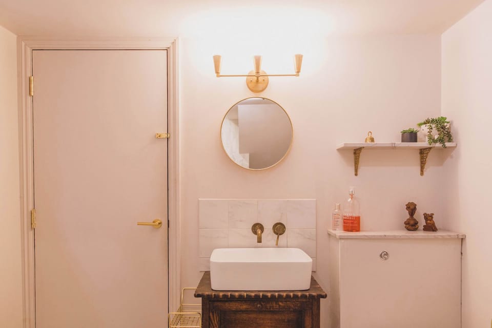 A bright and airy bathroom with gold fixtures, a round mirror, and minimalist decor.