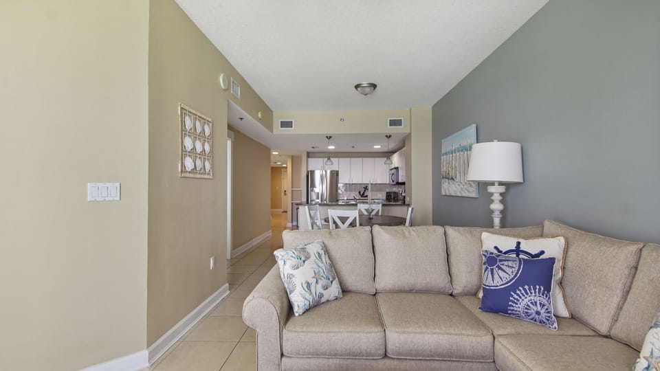 Open living area with a view into the kitchen featuring modern appliances and coastal decor.