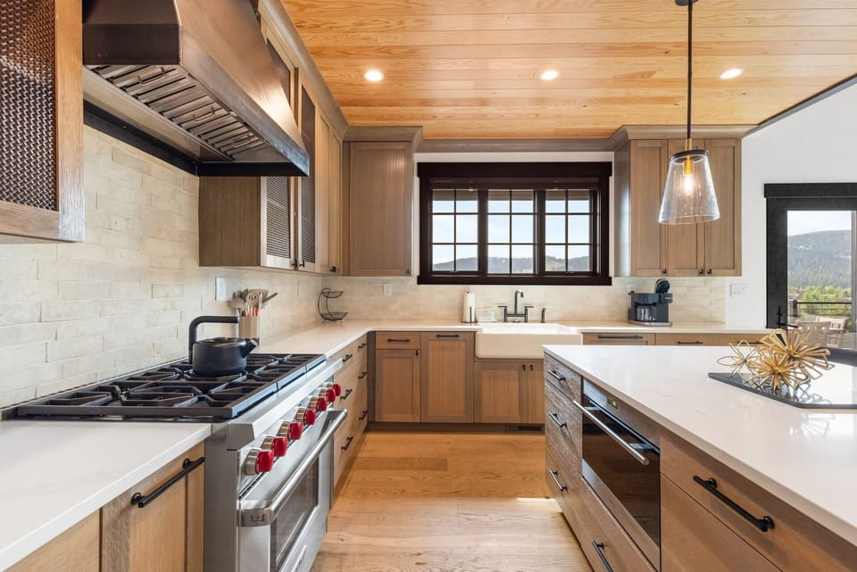 Step into your gourmet kitchen where warm wood tones meet modern convenience. The chef's gas range and farmhouse sink invite you to create memorable meals while natural mountain light streams through the window above your counters.