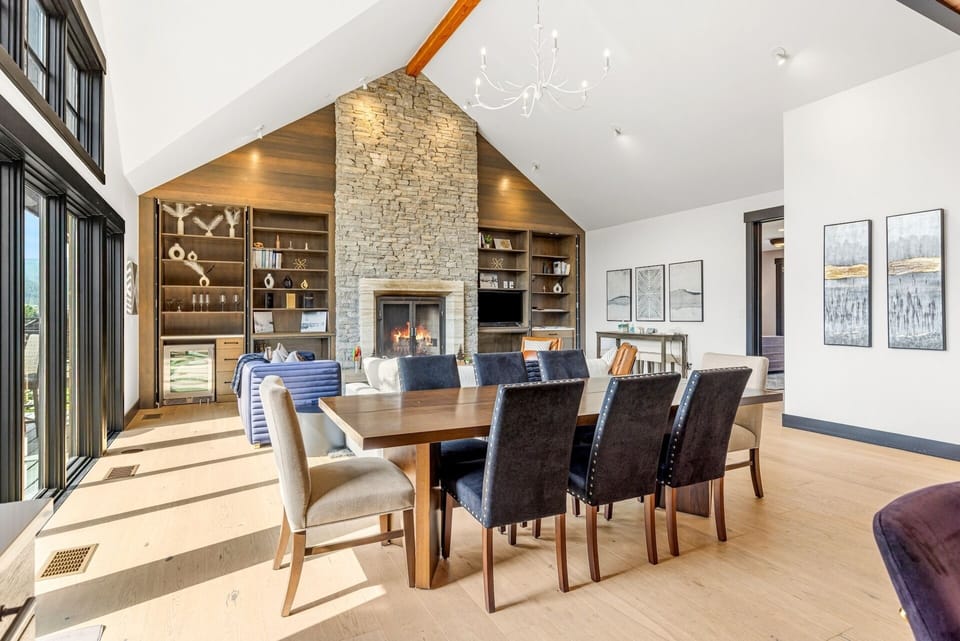 Gather around the elegant dining table beneath soaring vaulted ceilings, where the stone fireplace and warm wood accents create an inviting atmosphere for your meals together.