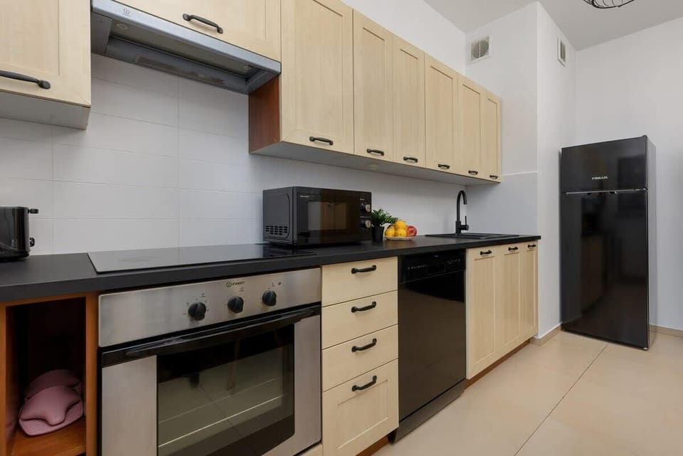 A well-organized kitchen with light wooden cabinets and black fixtures, offering a modern and practical cooking space.

