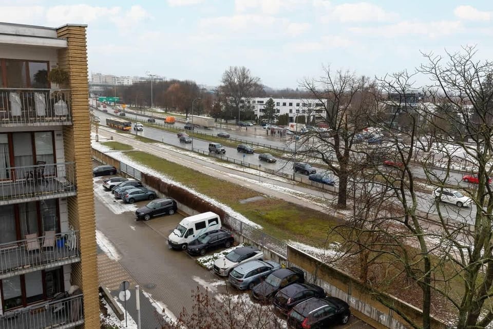 A panoramic view from the balcony overlooking a residential area with green spaces and parked cars.

