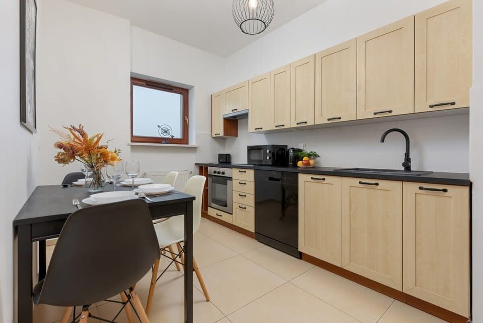 A modern kitchen with wooden cabinets, black countertops, and dining area, providing a functional and stylish cooking space.


