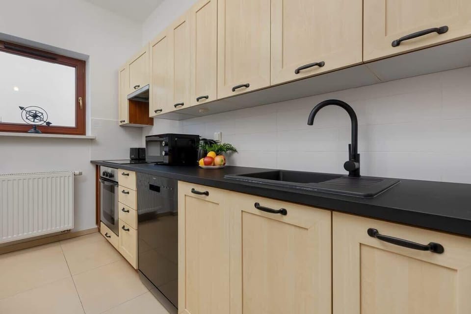 A well-organized kitchen with light wooden cabinets and black fixtures, offering a modern and practical cooking space.

