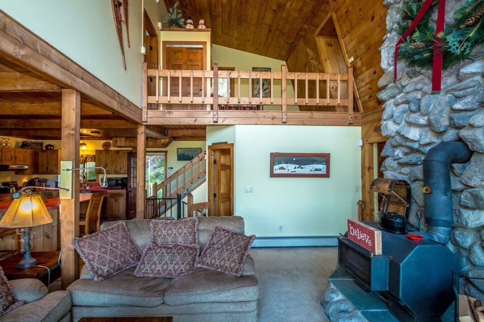 Cozy den with an open floor plan to the kitchen and dining area. Enjoy mountain views through sliders to the deck, a large wood stove for warmth, and a big-screen TV with streaming—perfect for unwinding.